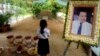 In this Nov. 20, 2016 photo, a girl stands by a portrait of Kem Ley, a Cambodian prominent political analyst, at his grave in Ang Takok, Cambodia. Kem Ley, a poor rice farmer's son turned champion of Cambodia's have-nots, was sipping his usual iced latte in the same chair he had occupied most mornings for years when a former solider he may never have met walked into the Caltex gas station cafe. Armed with a semi-automatic Glock pistol, the assassin fired into his chest and head, execution-style. Then he walked casually away from the scene. (AP Photo/Denis Gray)