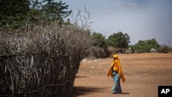FILE - In this Dec. 19, 2017 file photo, a Somali refugee girl walks past the fence surrounding a hut at Dadaab refugee camp, hosting over 230,000 inhabitants, in northern Kenya.