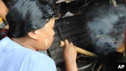 FILE - Fuel-efficient stoves use significantly less firewood than a traditional three-stone stove. This woman in Burma is using a pipe to help increase the fire's flames to cook the food.