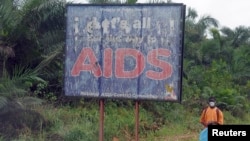 FILE - A man stands next to an AIDS billboard as he cleans a street in Yaounde, March 20, 2009. 