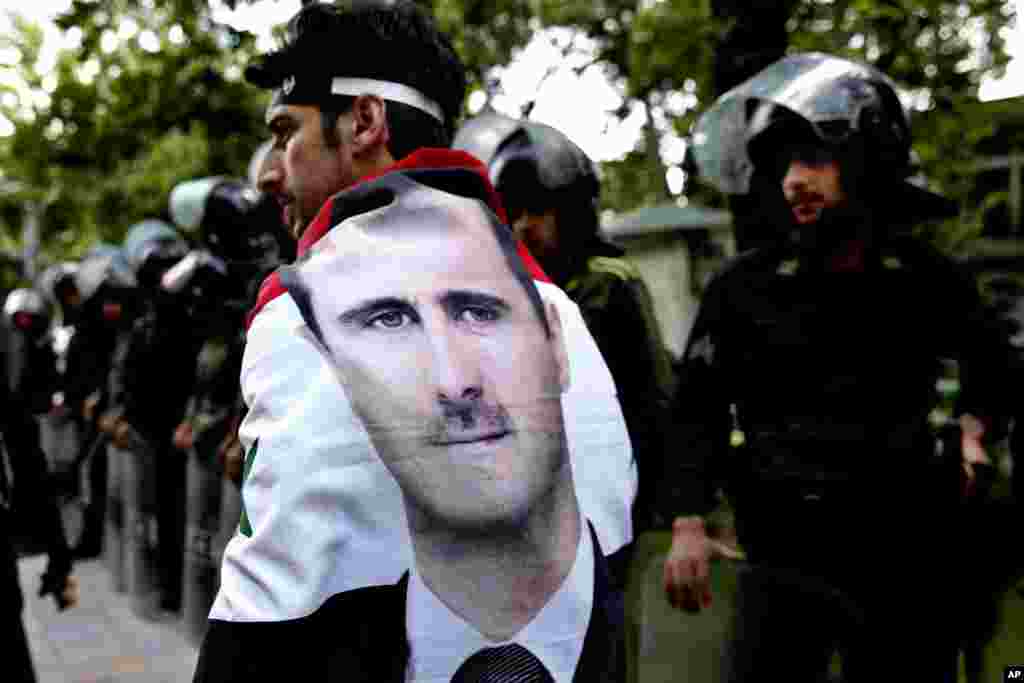 Seorang pria yang mengenakan bendera Suriah bergambar potret Presiden Bashar Assad, berjalan melewati polisi anti huru-hara Iran selama demonstrasi anti-Israel di depan kantor PBB di Teheran, Iran.