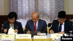 Government of the Philippines (GPH) chief negotiator Miriam Coronel Ferer (L) and Moro Islamic Liberation Front (MILF) chief negotiator Mohagher Iqbal (R) sign the peace agreement between both parties with AB Ghafar Tengku Mohamed as a witness from Malays